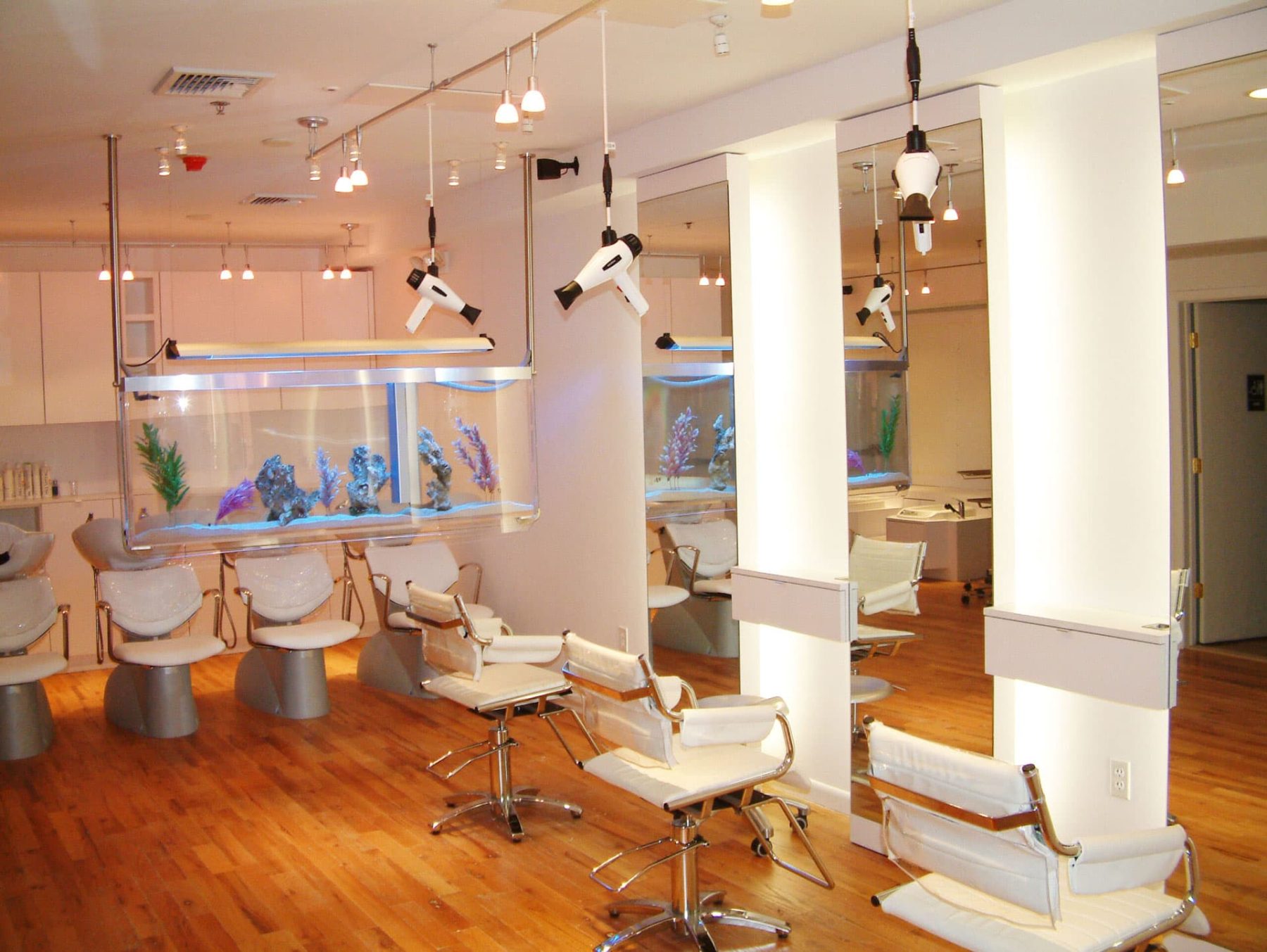 Modern salon interior with suspended Freestylist weightless blow dryers and a large aquarium centerpiece.